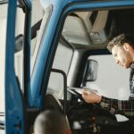 Man in Plaid Shirt Sitting in the Body of Blue Truck and Reading Papers