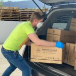 man in green t-shirt and blue denim jeans holding brown cardboard box