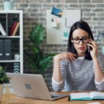 a woman sitting at a desk talking on a cell phone